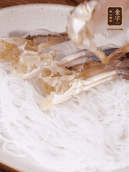 盤底墊上粉絲，擺上梭子蟹、火腿片，撒姜粒，淋上蒸魚豉油、花雕酒調(diào)味腌制15分鐘